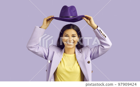 Cheerful stylish young woman holding hat over her head smiling broadly on colored background. 97909424