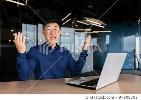 Successful asian businessman celebrating victory success, portrait of man in office in casual shirt, employee smiling and looking at camera satisfied with achievement holding hand up victory gesture. Successful asian businessman celebrating victory success, portrait of man in office in casual shirt, employee smiling and looking at camera satisfied with achievement holding hand up victory gesture. 97909502