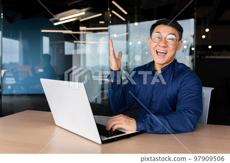 Successful asian businessman celebrating victory success, portrait of man in office in casual shirt, employee smiling and looking at camera satisfied with achievement holding hand up victory gesture. Successful asian businessman celebrating victory success, portrait of man in office in casual shirt, employee smiling and looking at camera satisfied with achievement holding hand up victory gesture. 97909506