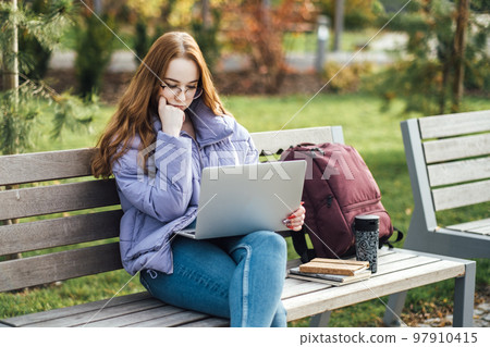 Choosing a university, college. Female college student with books and laptop outdoors. Redhead college student girl with glasses on campus 97910415