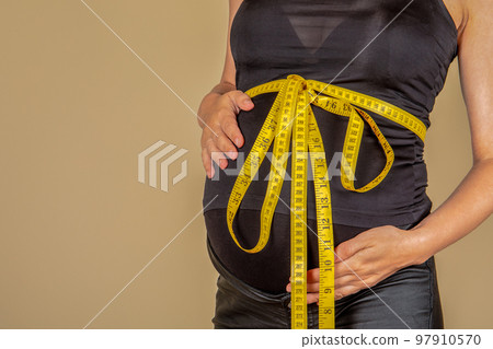 Pregnant woman. Measuring tape tied around a big belly Pregnant woman. Measuring tape tied around a big belly 97910570