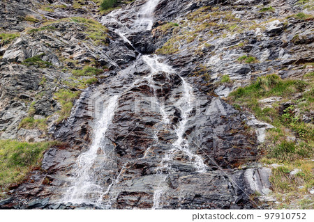 Granite alpine rocks along which a small mountain waterfall flows and foams 97910752