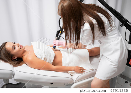 Beautician performing laser resurfacing of abdomen, ridding client of stretched skin. Fractional CO2 laser is modern device for treatment of skin defects, scars and stretch marks after childbirth. 97911286