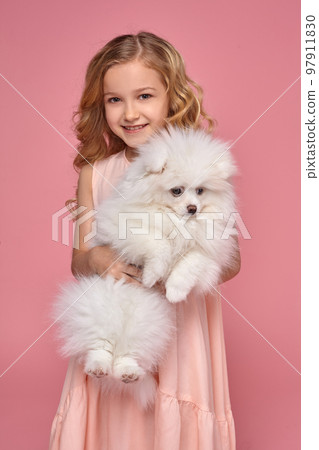 Little girl with a blond curly hair, in a pink dress plays with her dog 97911830