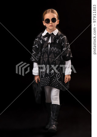 Little girl in a black glasses, dark poncho, black boots and a clutch in her hand Little girl in a black glasses, dark poncho, black boots and a clutch in her hand 97911883