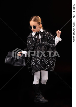 Little girl in a black glasses, dark poncho, black boots and a clutch in her hand Little girl in a black glasses, dark poncho, black boots and a clutch in her hand 97911897