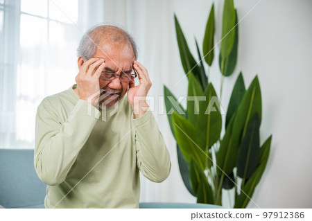 Headache. Sad Asian senior man sitting on sofa feeling hurt and lonely, elderly holds head with hand suffering from migraine headache, Old age health problems, healthcare Headache. Sad Asian senior man sitting on sofa feeling hurt and lonely, elderly holds head with hand suffering from migraine headache, Old age health problems, healthcare 97912386