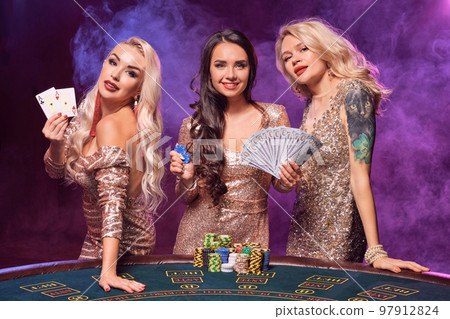 Beautiful girls with a perfect hairstyles and bright make-up are posing standing at a gambling table. Casino, poker. Beautiful girls with a perfect hairstyles and bright make-up are posing standing at a gambling table. Casino, poker. 97912824
