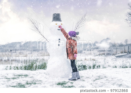Little girl adding a carrot for the snowman nose Little girl adding a carrot for the snowman nose 97912868