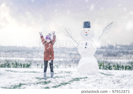 Girl cheering with a snowman in the snow Girl cheering with a snowman in the snow 97912871