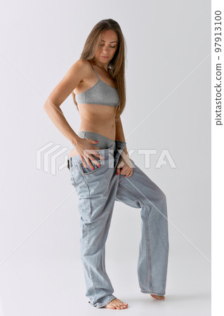 Full-length portrait of slim woman posing in top and jeans over grey studio background. Casual look 97913100