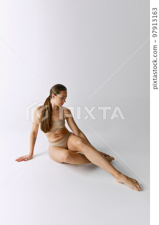 Full-length portrait of beautiful woman posing in beige underwear over grey studio background. Slender body Full-length portrait of beautiful woman posing in beige underwear over grey studio background. Slender body 97913163
