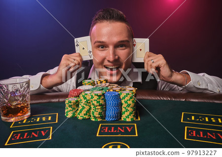 Wealthy man is posing at a poker table with chips and a glass of whiskey on it at a casino. Wealthy man is posing at a poker table with chips and a glass of whiskey on it at a casino. 97913227