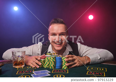 Wealthy man is posing at a poker table with chips and a glass of whiskey on it at a casino. Wealthy man is posing at a poker table with chips and a glass of whiskey on it at a casino. 97913229