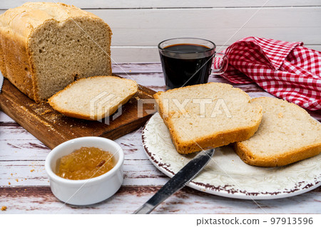 Overhead view of a homemade bread, slices and some sweet in a pot on a rustic tableNormal view of a homemade bread made with a bread machine, slices on a plate and some sweet in a pot on a table 97913596