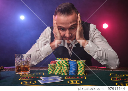 Wealthy man is posing at a poker table with chips and a glass of whiskey on it at a casino. Wealthy man is posing at a poker table with chips and a glass of whiskey on it at a casino. 97913644