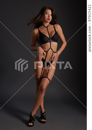 Beautiful woman in underwear and leather bandage posing against dark grey background. Beautiful woman in underwear and leather bandage posing against dark grey background. 97915421