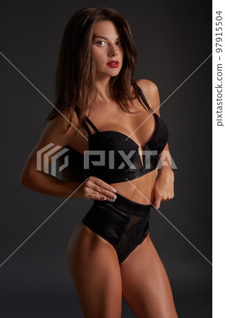 Slim and beautiful woman with dark straight hair, and bronzed skin is posing in the black basic underwear collection on the dark grey background 97915504