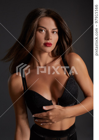 Stunning caucasian female model with dark hair and red lips in black underwear posing on dark grey background. Stunning caucasian female model with dark hair and red lips in black underwear posing on dark grey background. 97915566