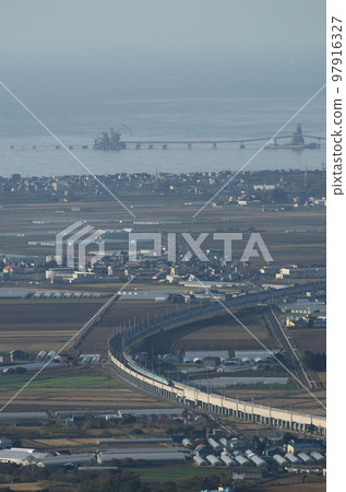 The Hokkaido Shinkansen running with the cement factory pier jutting out into Hakodate Bay in the background 97916327