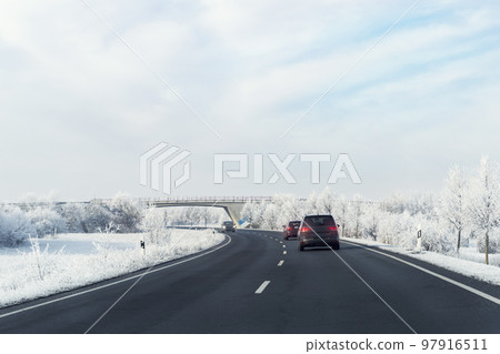 Scenic view clean intercity highway road drive cars with beautiful white covered snow trees blue sky on background at bright cold sunny day. Urban cold snowy day snowstrom town background 97916511