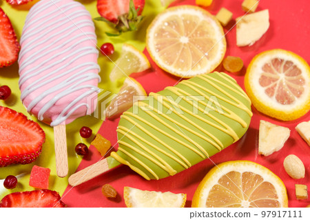 Two ice creams on a sticks - strawberry and lemon on a yellow and red background. Summer fruit desserts. Two ice creams on a sticks - strawberry and lemon on a yellow and red background. Summer fruit desserts. 97917111