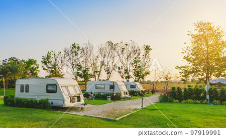 Cozy retro travel trailer Caravan on green grass before sunset near riverside in peaceful countryside. Family vacation travel RV, holiday trip in motorhome. Outdoor and Recreational Vehicles Theme. Cozy retro travel trailer Caravan on green grass before sunset near riverside in peaceful countryside. Family vacation travel RV, holiday trip in motorhome. Outdoor and Recreational Vehicles Theme. 97919991