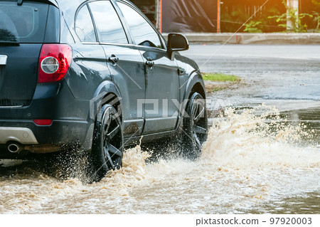 Car passing through a flooded road. Driving car on flooded road during flood caused by torrential rains. Flooded city road with a large puddle. Splash by car through flood water. Selective focus. 97920003
