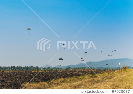 Army cadet paratroopers in military uniform landing on field. Skydiver paratrooper in parachute dome lands in the set area to land situated in the field among the soil. Military parachuting training. 97920087