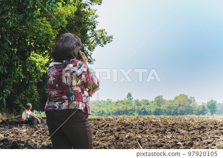 Back view of Asian elderly woman farmer use phone for business to plan farming in wilderness. Female farmers consult with landowners to cultivate crops in soil field. Farm and agricultural business. 97920105