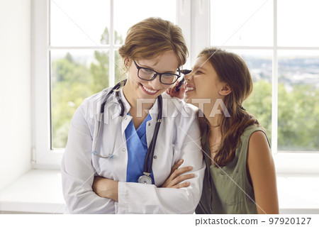 Funny teenage girl having fun looking through otoscope at ear of friendly female doctor. 97920127