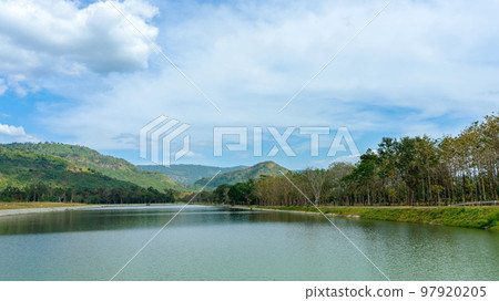 Beautiful and peaceful view of large reservoir with surrounding mountain and trees in beautiful sunshine and cloudy sky in Thailand. Tranquil and beautiful natural scenery landscape of reservoir lake. 97920205