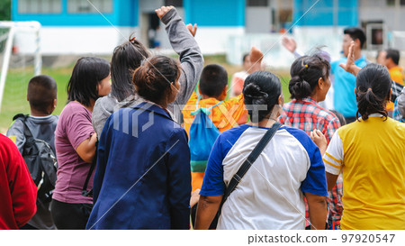 Back view of Moms watch and cheering their sons playing football in school tournament on sideline. Sport, outdoor active,  Spectator watching soccer game. Parents care and encourage their children. 97920547