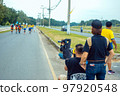 Back view of Asian sport photographer with camera sit to take picture marathon runners in running event marathon run on city street with blurred image of runners in background. Sports and photography. 97920548
