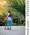 Asian woman enjoy playing and riding modern extreme stunt kick scooter without using any safety gear in home. Active sport lifestyle of young female in nature. Happy woman ride scooter without helmet. 97920556