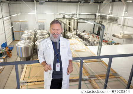 Contented factory technologist posing for the camera against big vats 97920844