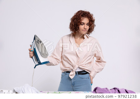 The girl is boiling with anger that she has to iron men's shirts again. The girl is boiling with anger that she has to iron men's shirts again. 97921238