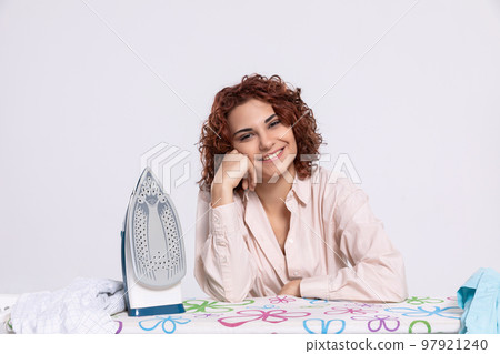 A smiling woman sits at the ironing board and iron. A smiling woman sits at the ironing board and iron. 97921240