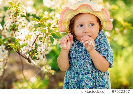 a little girl in a hat by a flowering tree in a spring garden 97922207
