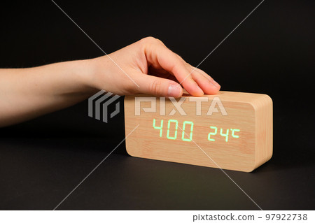A digital clock showing a time of four o'clock in the morning and a woman's hand on a black background 97922738