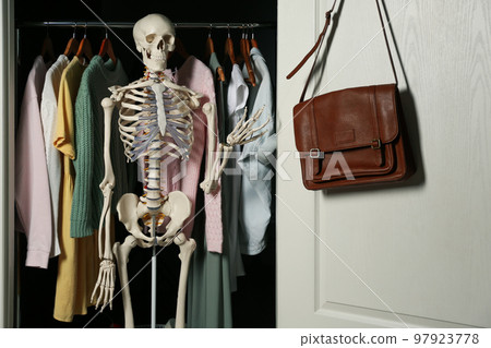 Artificial human skeleton model among clothes in wardrobe 97923778