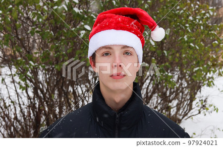 Closeup portrait of teen boy wearing santa hat in winter. 97924021