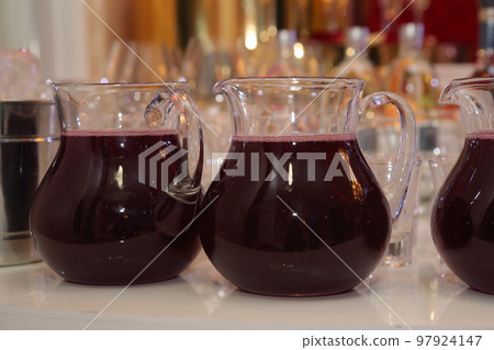 glass jar with morse red fruit drink and wine glasses closeup photo 97924147