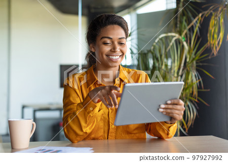 Modern technologies in business. Happy black businesswoman using modern digital tablet, working online in office Modern technologies in business. Happy black businesswoman using modern digital tablet, working online in office 97927992