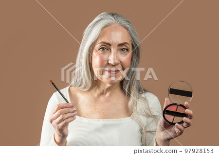 Cheerful senior european lady with gray hair shows cosmetics, blush or eye shadow with brush 97928153