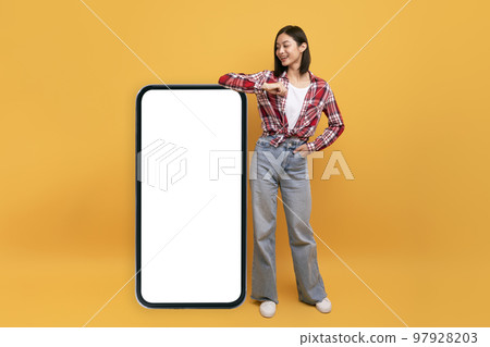 Happy japanese lady leaning on big smartphone with blank white screen and smiling, yellow studio background, mockup Happy japanese lady leaning on big smartphone with blank white screen and smiling, yellow studio background, mockup 97928203