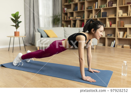 Young asian lady doing domestic training on yoga mat, standing in plank, strengthening abs muscles at home, free space Young asian lady doing domestic training on yoga mat, standing in plank, strengthening abs muscles at home, free space 97928252