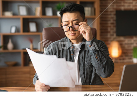Serious concentrated mature japanese man boss in glasses works with documents at workplace in office Serious concentrated mature japanese man boss in glasses works with documents at workplace in office 97928253