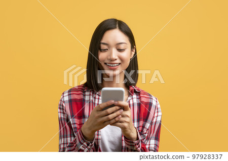 Young asian woman using smartphone for messaging, smiling lady texting on cellphone, yellow background, free space Young asian woman using smartphone for messaging, smiling lady texting on cellphone, yellow background, free space 97928337