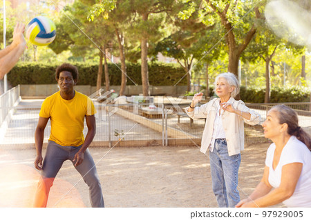 Joyful multiracial group of mature adult people playing volleyball game outdoors 97929005